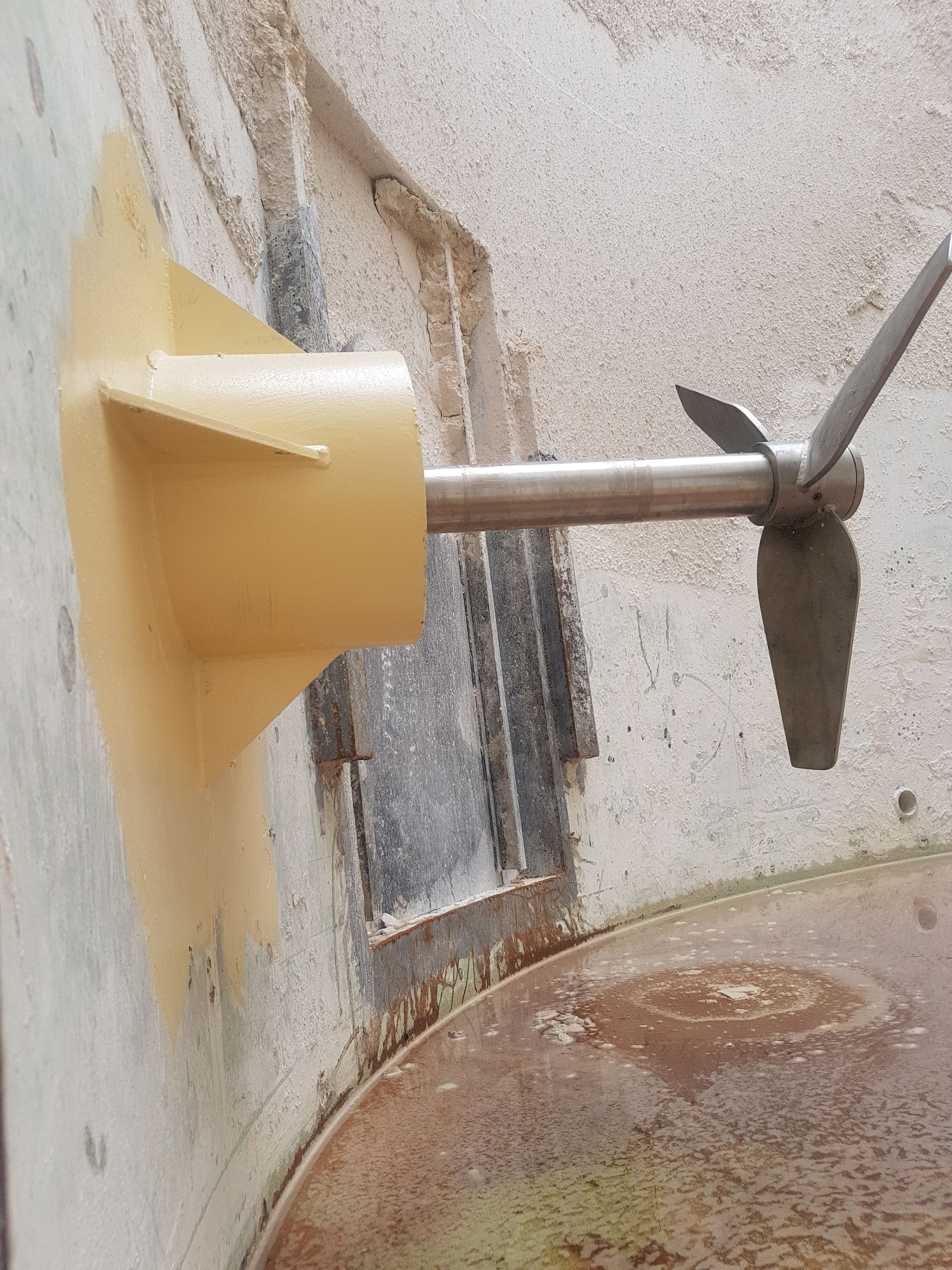 A side entry mixer mounted to the tank, viewed from the inside so the impeller is visible and the interior of the tank.